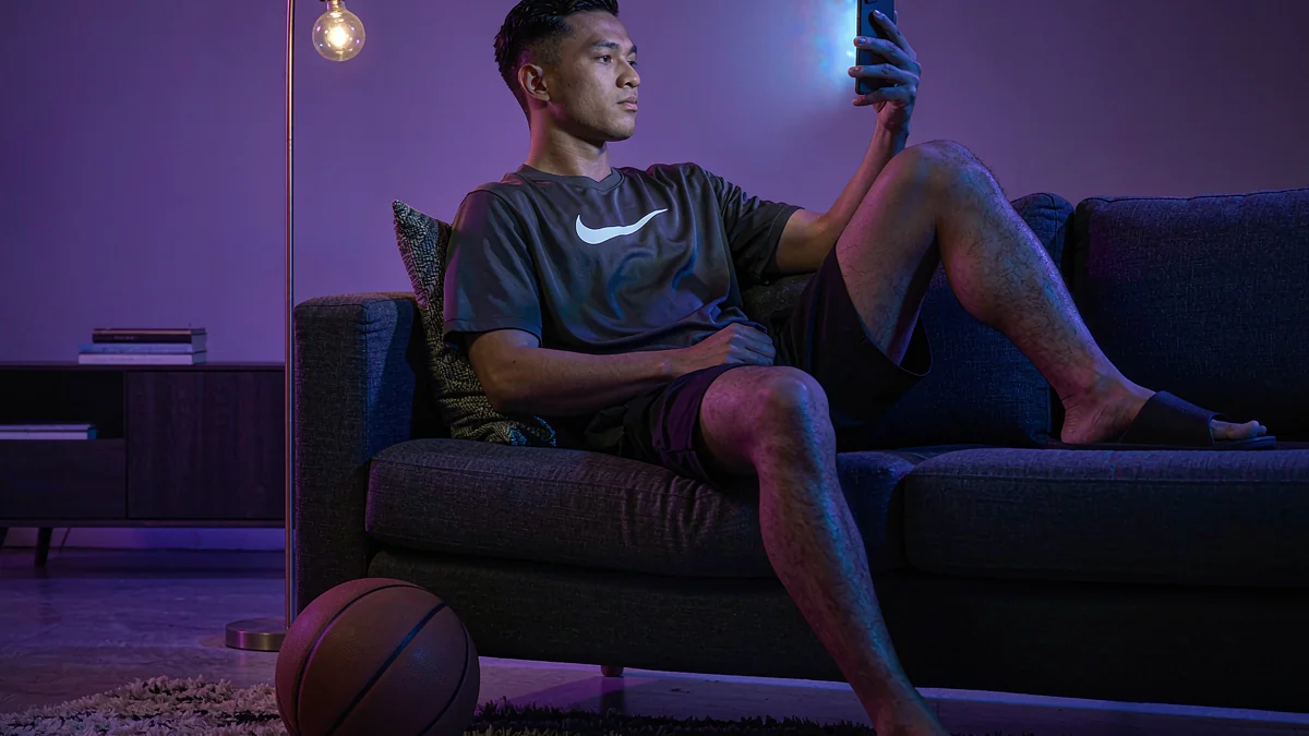 An adult spectator looking at a phone while seated on a sofa — L444 guide
